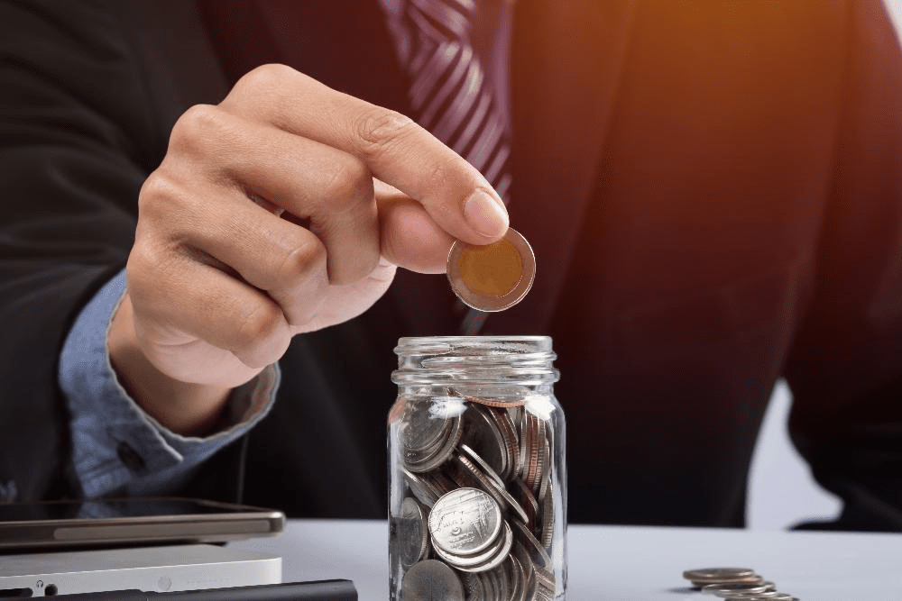 Photo shows man adding a coin to a savings coin jar